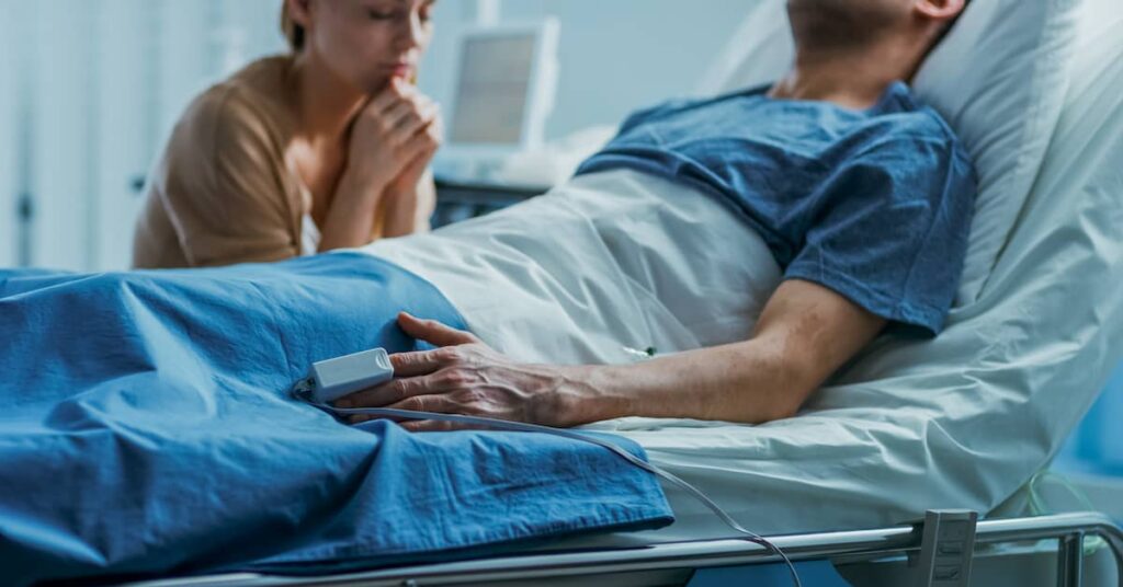 Man lies in hospital bed with woman at the bedside. | Colling Gilbert Wright medical malpractice lawyer