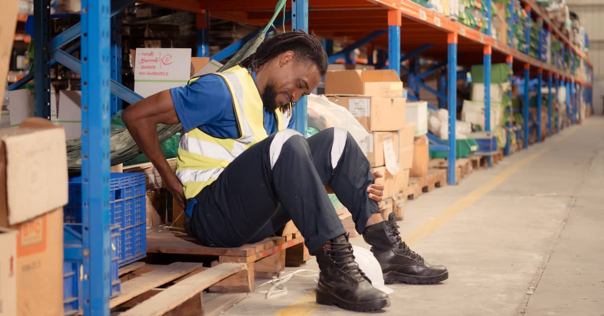 Worker in a warehouse clutching his back in pain. | Colling Gilbert Wright