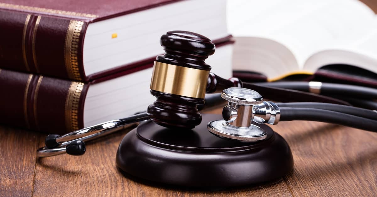 A gavel and stethoscope sit next to law books. | Colling Gilbert Wright