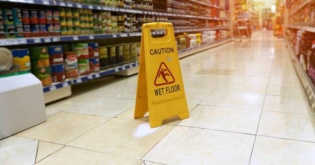 Caution wet floor sign in supermarket aisle. | Colling Gilbert Wright